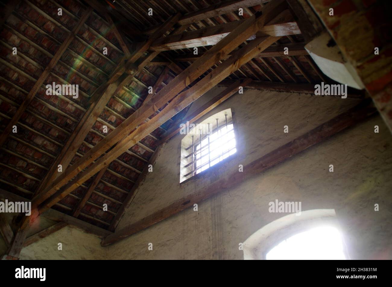 Mansarda dimenticata. La luce del sole splende da una finestra in un vecchio edificio. Interni abbandonati con travi in legno. Foto Stock