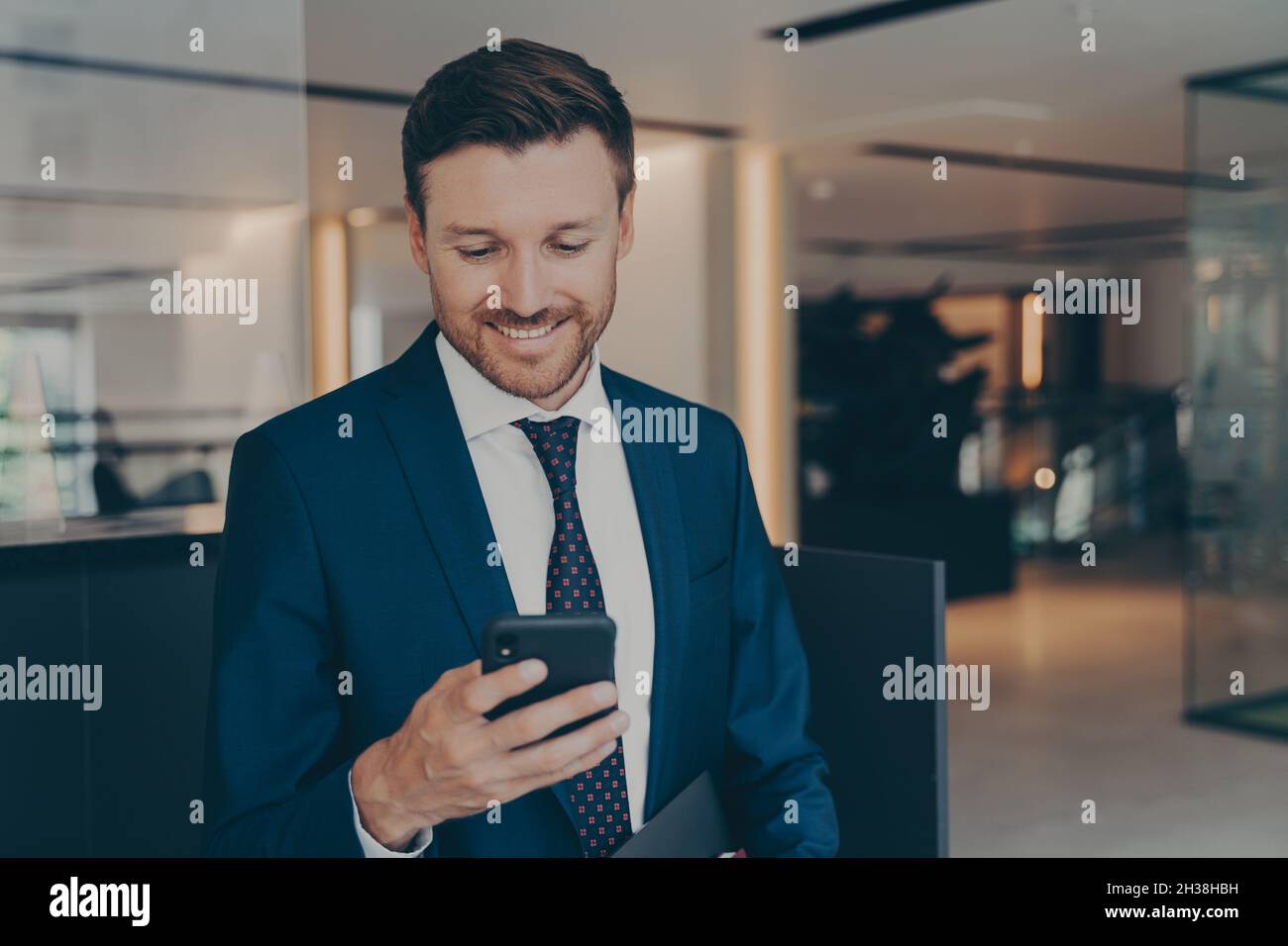 Felice giovane impreditore utilizzando smart phone in piedi nel corridoio di office Foto Stock
