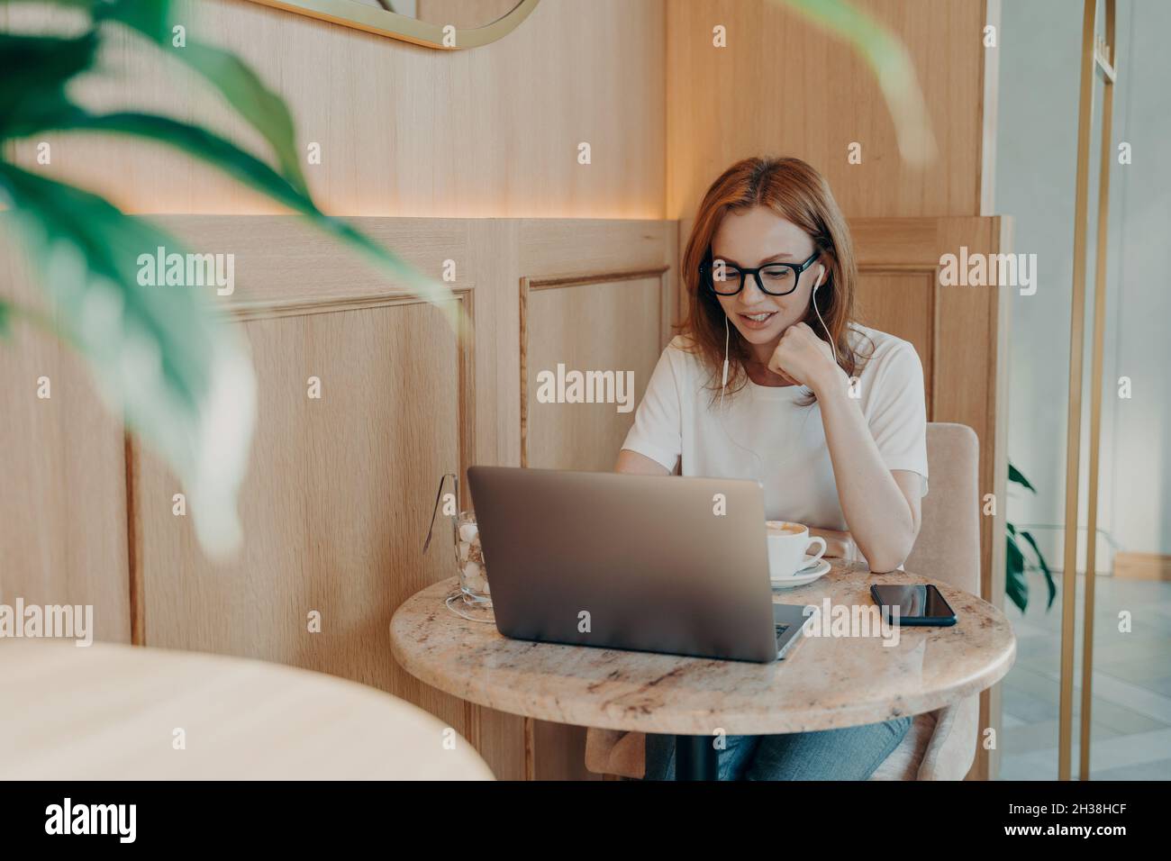 Giovane ragazza bella rossa-capelli freelance donna in auricolari funziona a distanza sul laptop in caffetteria Foto Stock