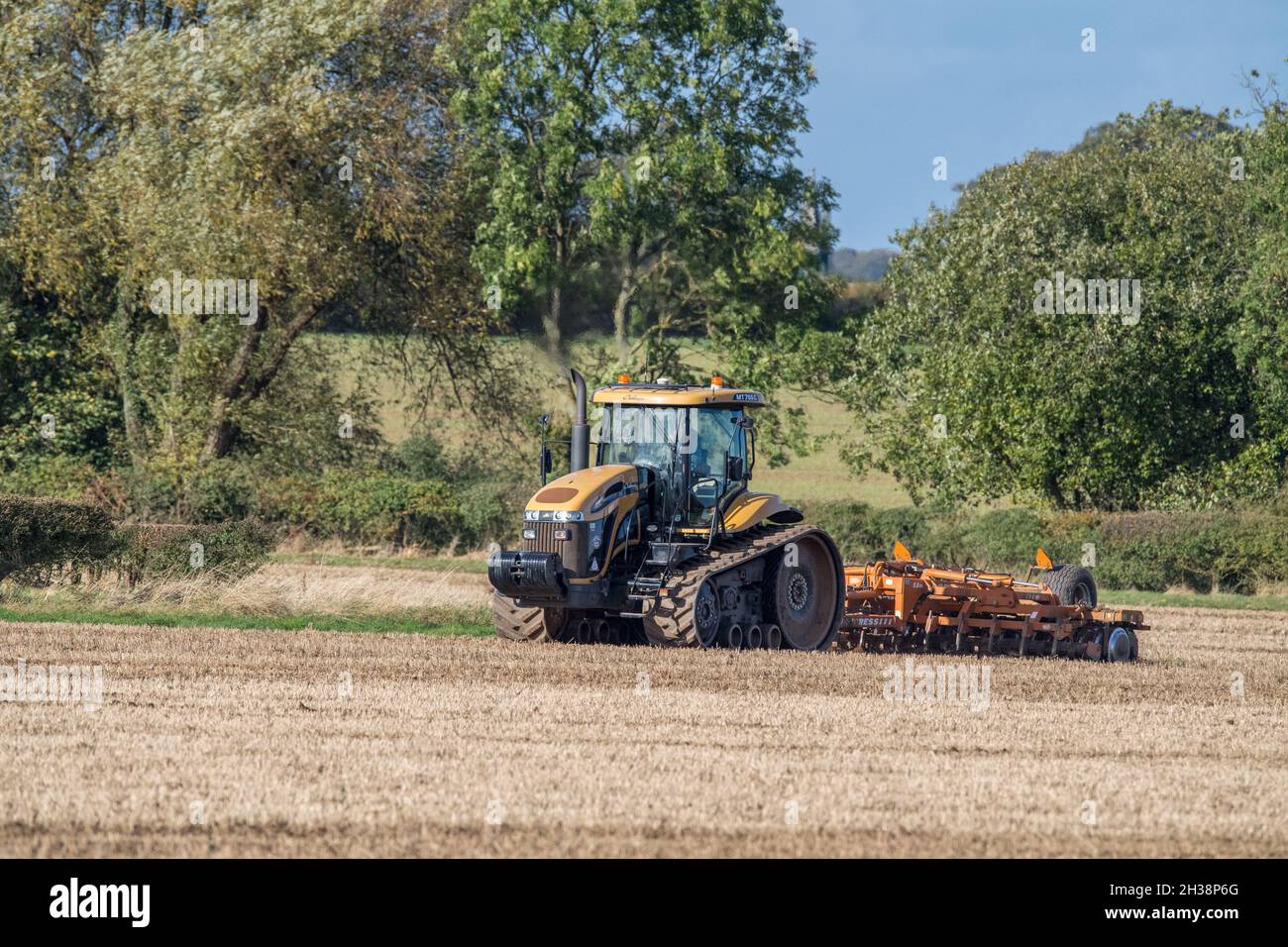 Agricoltore che utilizza un trattore cingolato agricolo Challenger e che traina una pressa per colture da 5,5m su un campo. Foto Stock
