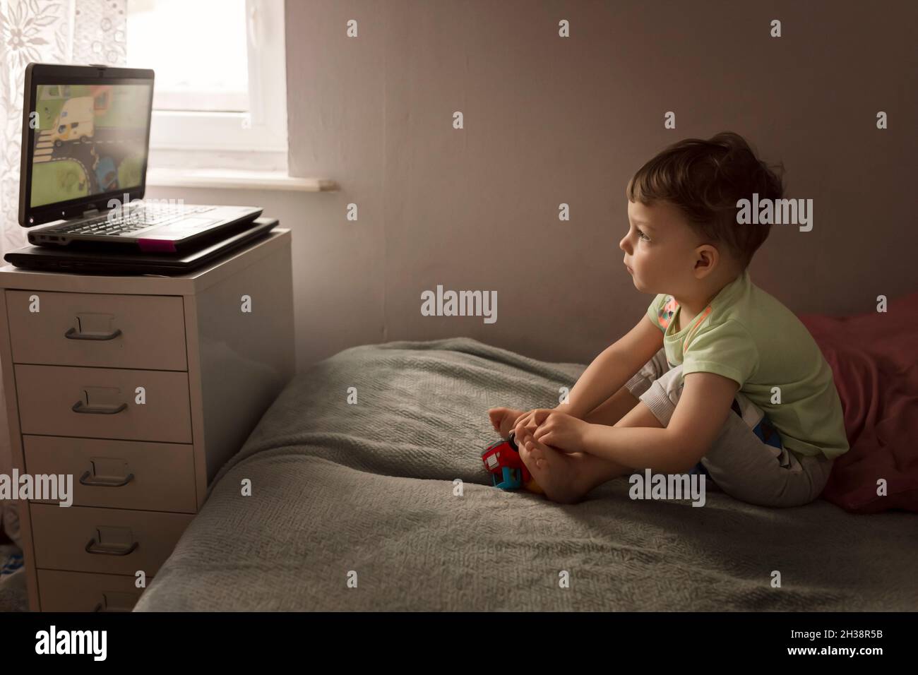 Ragazzo del bambino seduto sul letto e guardando i cartoni animati sul computer portatile Foto Stock
