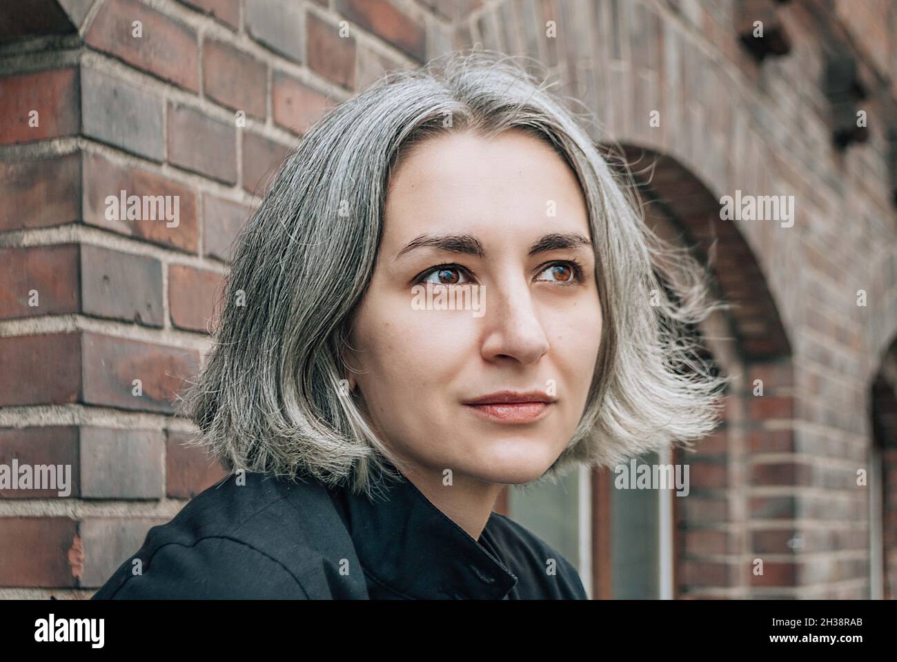 La donna dai capelli grigi guarda via sul retro dell'edificio in mattoni Foto Stock