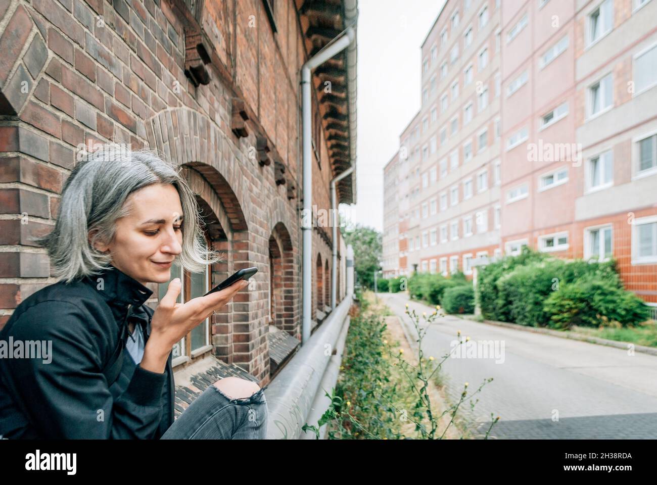 Una donna dai capelli grigi comunica sullo smartphone tramite messaggi vocali Foto Stock