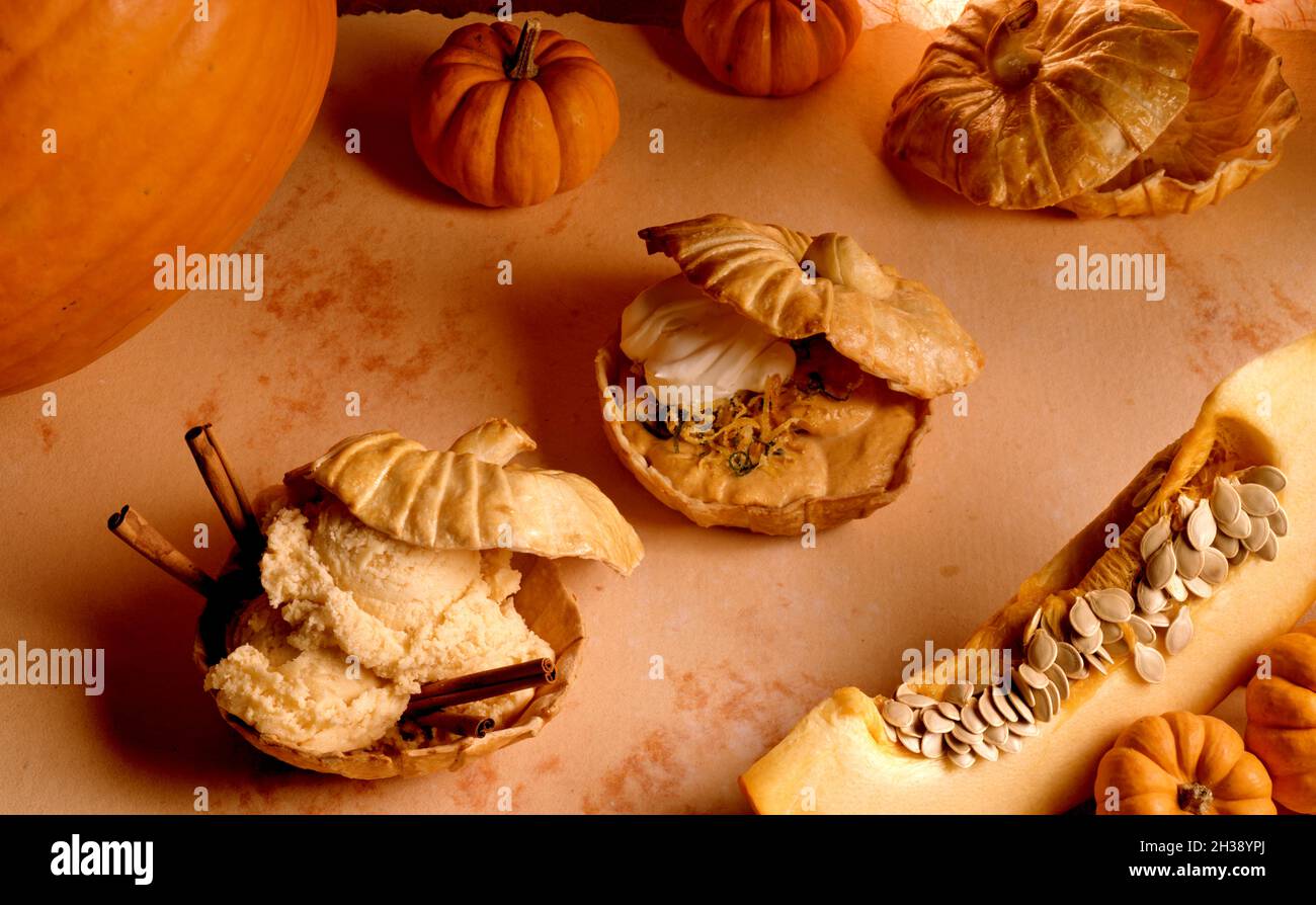 Conchiglie di pasticceria a forma di zucche, riempite di gelato alla zucca, mousse di zucca, tutte circondate da zucche fresche di varie dimensioni. Foto Stock