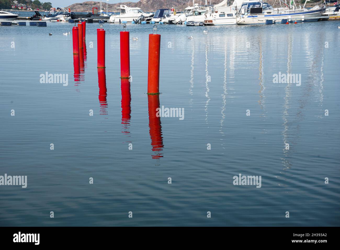 Paletti rossi nell'acqua di mare con un porto di barche sullo sfondo Foto Stock