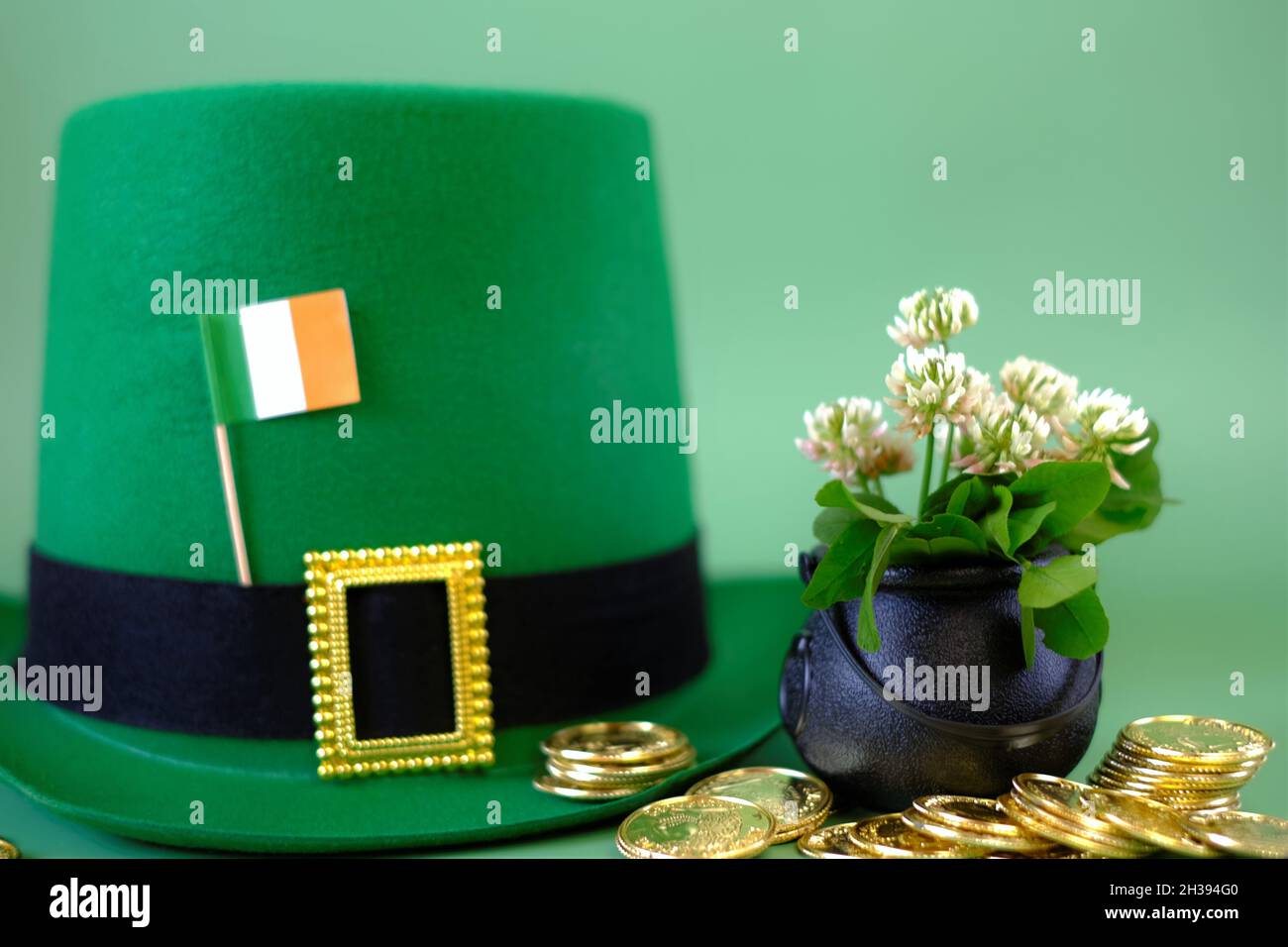 Giorno di San Patrizio. Cappello leprechaun, bandiera d'Irlanda, cappello bowler con monete d'oro, mazzo di chiodi di garofano su sfondo verde. Festa di San Patrizio. St Foto Stock