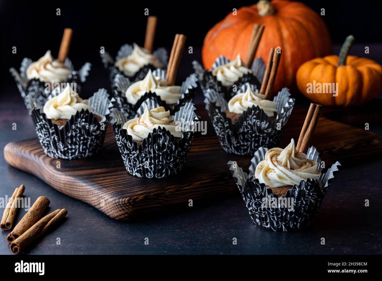 Cupcake di zucca speziata e bastoncini di cannella per guarnire su sfondo scuro Foto Stock