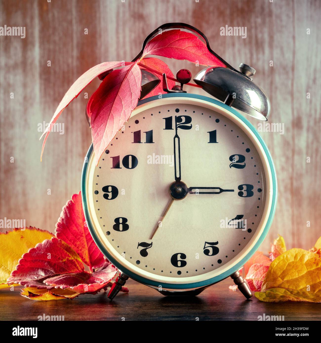 Ora legale, ritorno di un'ora in autunno. Una sveglia retrò con foglie autunnali su un rustico sfondo di legno Foto Stock