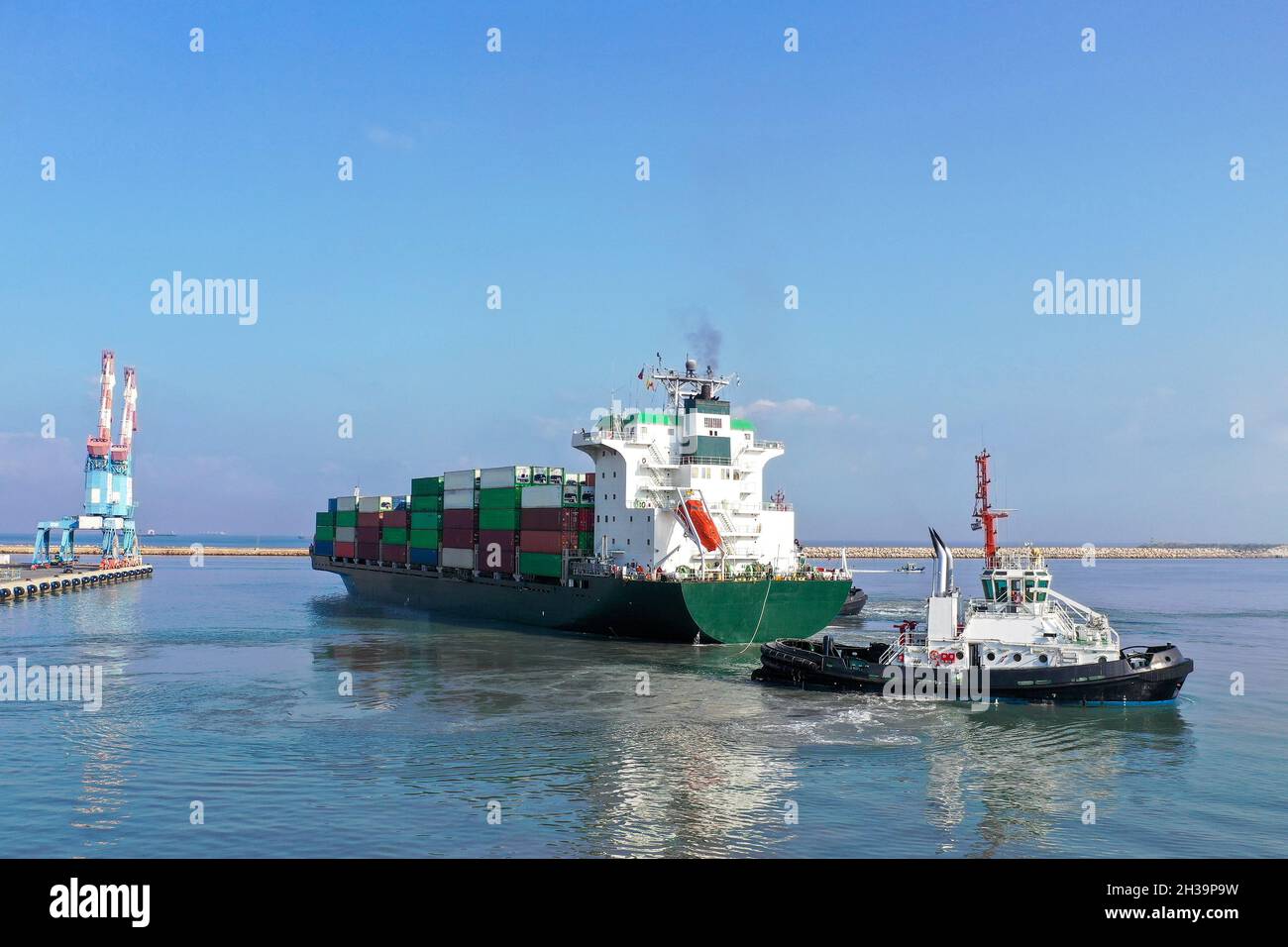 Rimorchiatori che dirigono una nave container in un molo portuale. Foto Stock