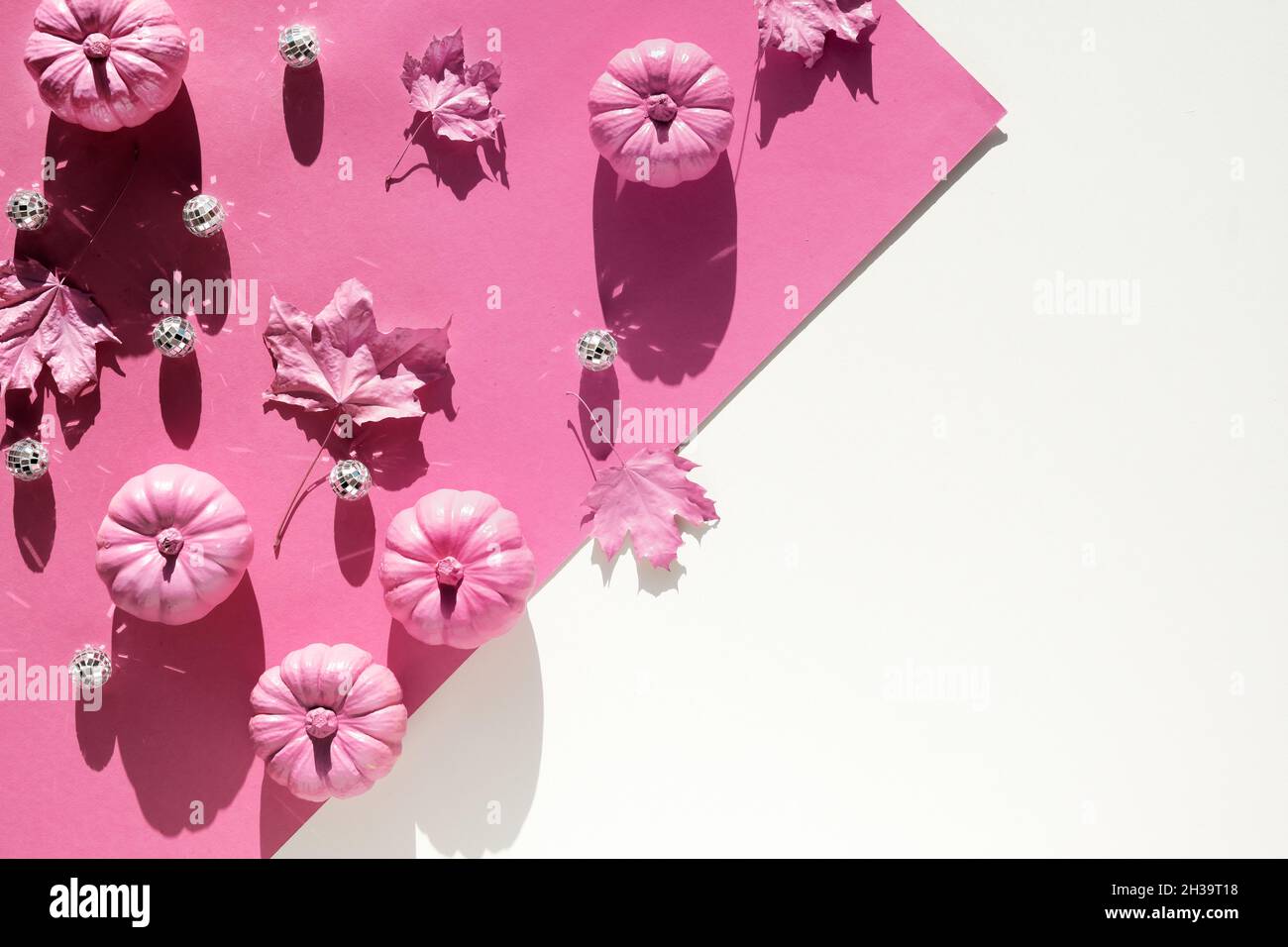Sfondo di carta rosa fucsia con decorazioni autunnali. Aspetto monocromatico con zucche rosa e femmina mano tenuta cadere foglie secche dipinte di rosa. Magenta Foto Stock