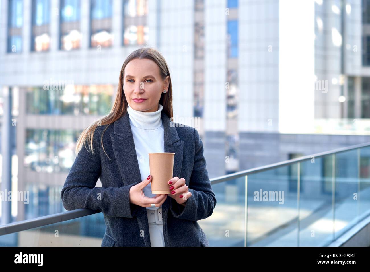 donna d'affari in giacca con caffè in mano si alza sulla terrazza del centro business. profondità di campo poco profonda Foto Stock