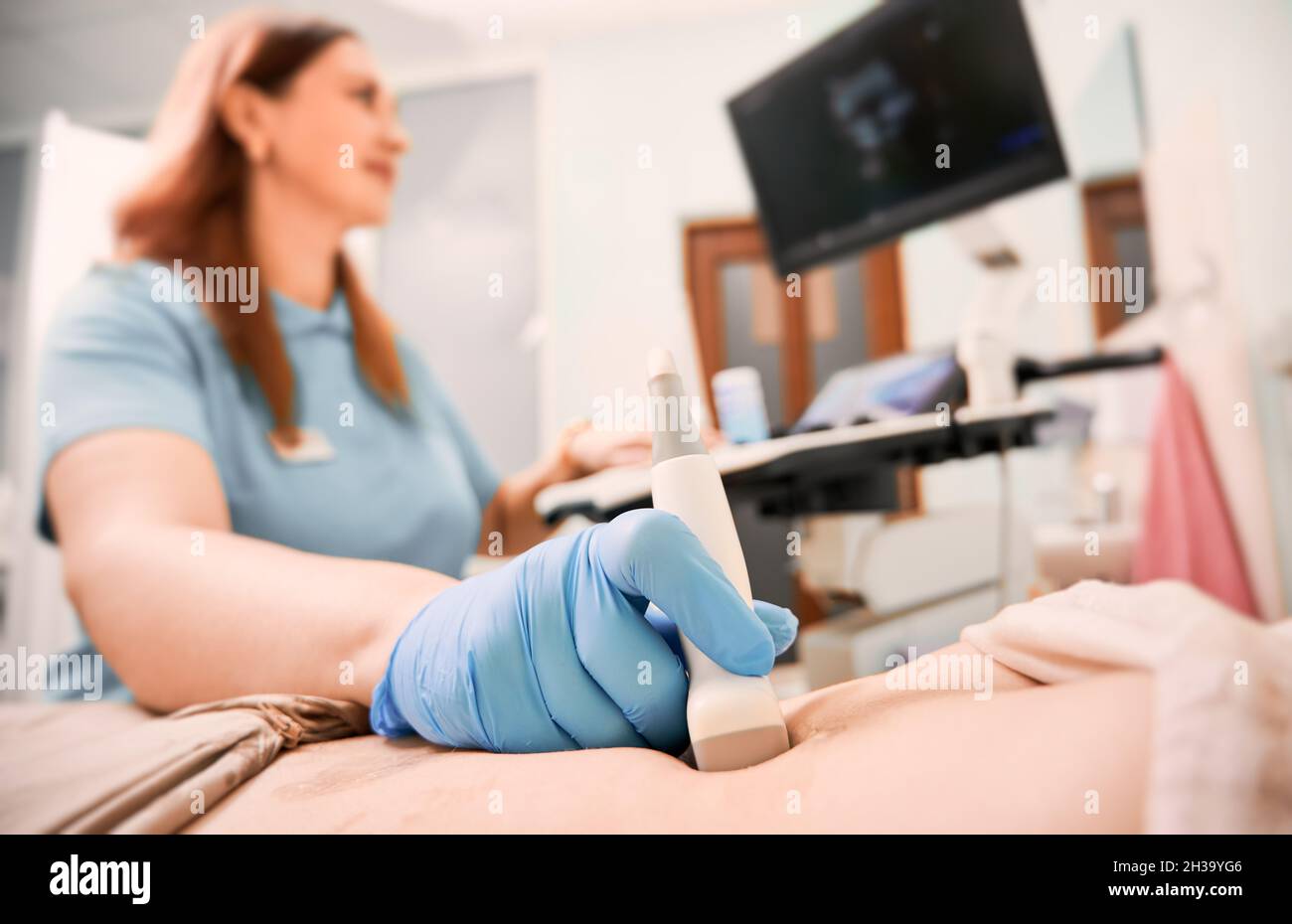 Concentratevi sulla mano del sonografo in guanto sterile che esamina la donna con scanner a ultrasuoni. Medico di sesso femminile che sposta il trasduttore sull'addome del paziente guardando il display. Concetto di diagnostica a ultrasuoni. Foto Stock