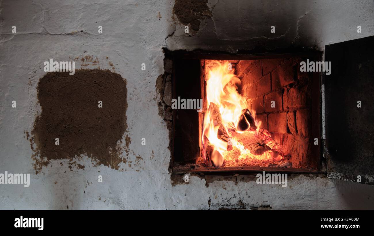 Un fuoco sta bruciando in Una stufa del villaggio del mattone. Fiamme, carboni caldi e tronchi. Foto Stock