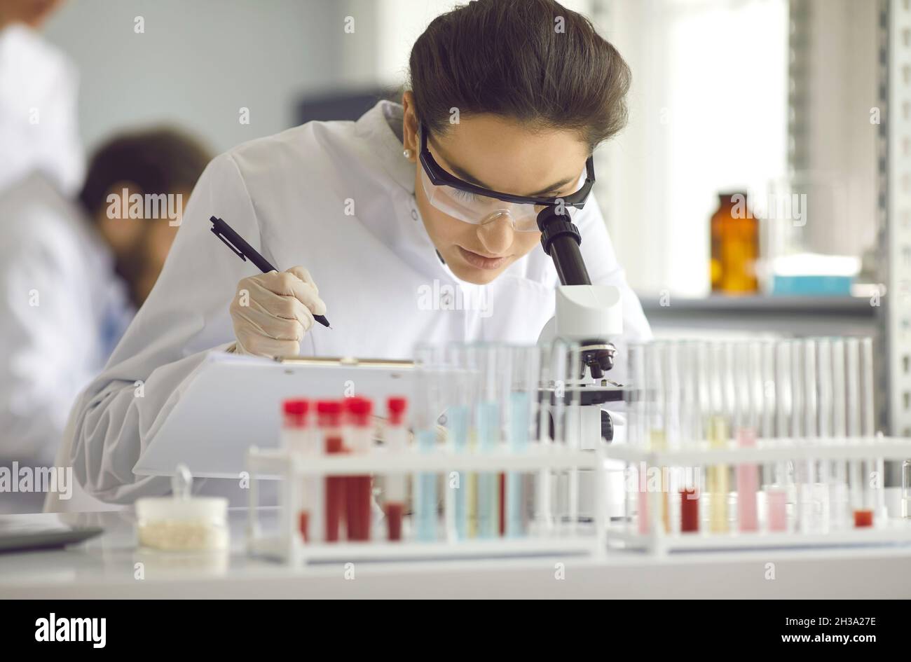 Donna in un cappotto bianco guarda al microscopio. Foto Stock