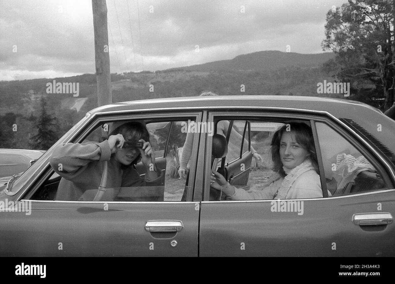 1978 Blue Mountains, Australia: A Year 12 (6th form) adolescente (ragazza/donne) studente di scuola scatta una foto del fotografo utilizzando una fotocamera istamatica tasca film 110 mentre un altro studente guarda sopra. L'auto nella foto è una Mazda Capella Foto Stock