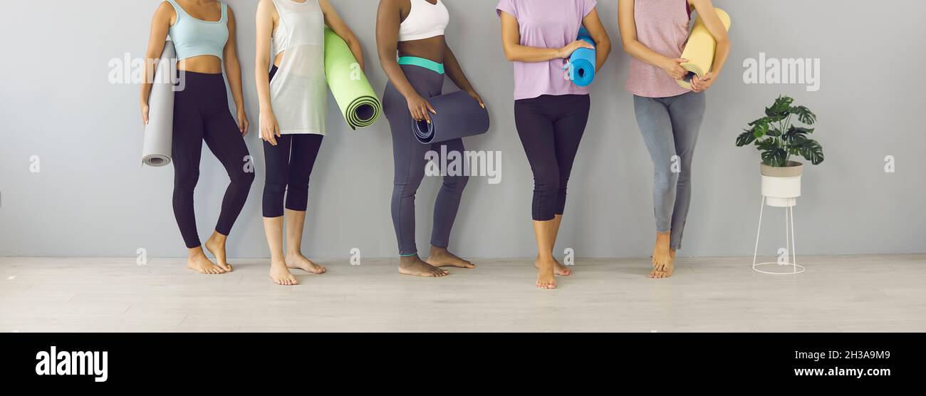Banner con sezione bassa di donne in pantaloni yoga in piedi da parete e tenendo materassini palestra Foto Stock