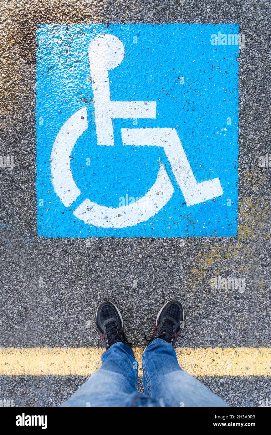 Un uomo in piedi di fronte al simbolo sui ciottoli nell'area riservata ai parcheggi per disabili Foto Stock