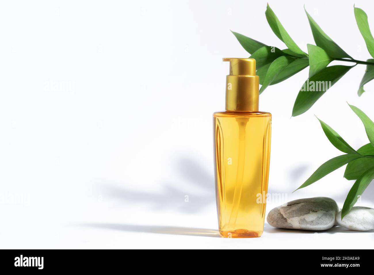 Bottiglia trasparente di olio arancione giallo per proteggere il sole, abbronzarsi o i capelli. Sfondo bianco con ombre, piante e pietre dure. Cosmetici per la cura estiva. C Foto Stock