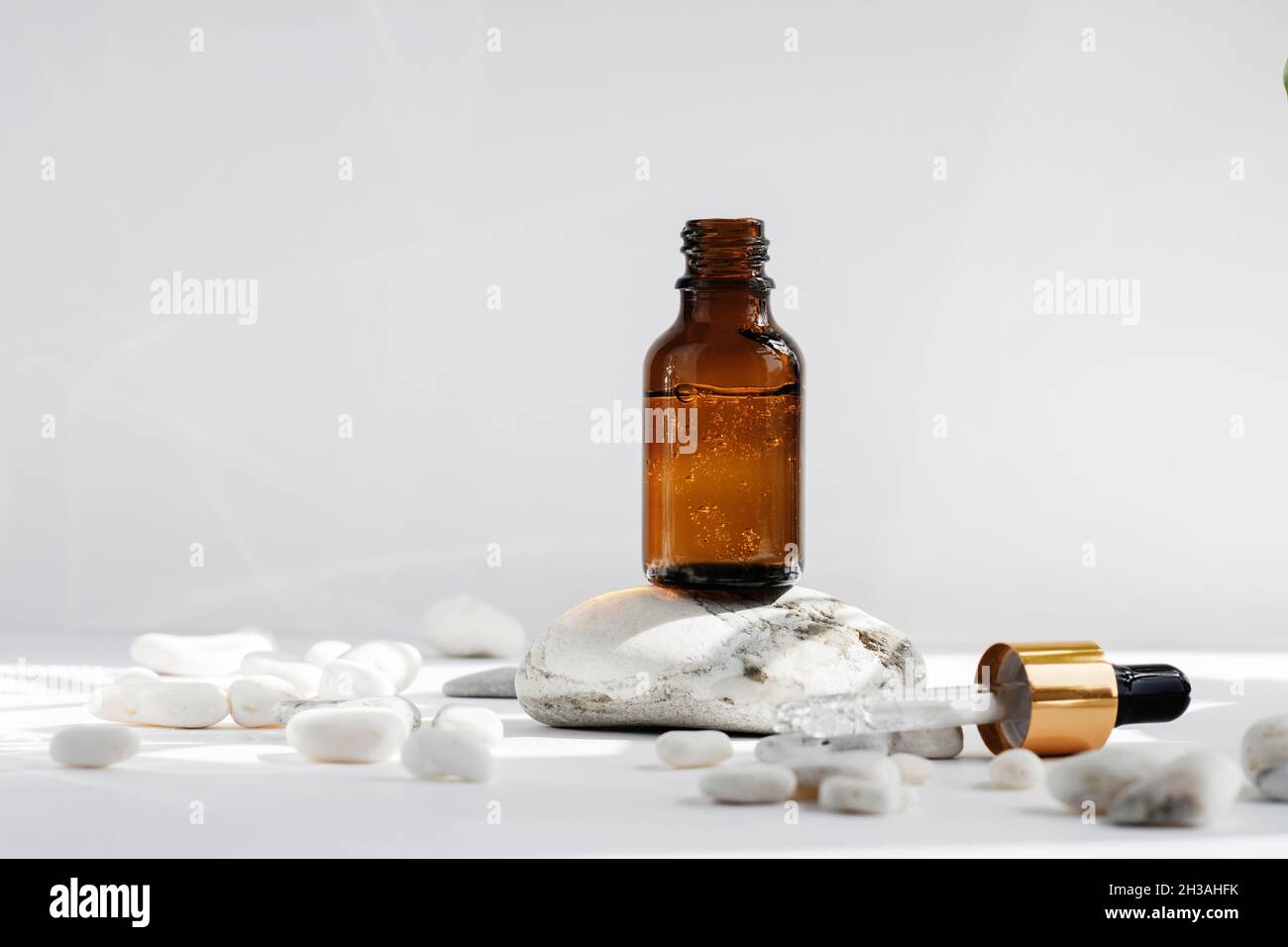 Beffa di una bottiglia aperta in vetro su un podio in pietra su uno sfondo bianco grigio con ombre e pietre dure. Ombre dure. Pipetta cosmetica su un Foto Stock