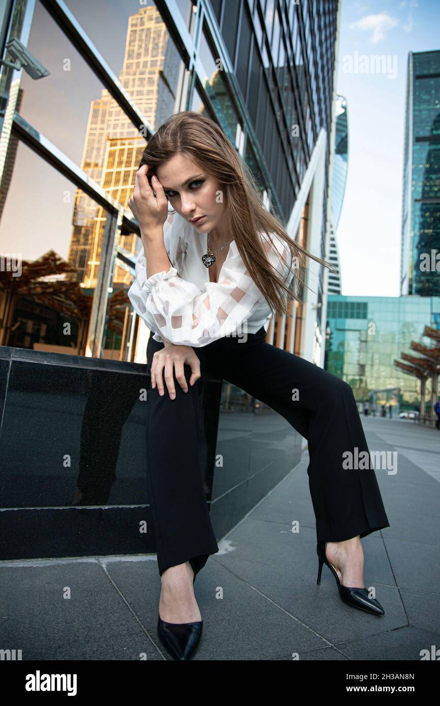 Giovane donna d'affari nella città moderna di skyscapers con capelli lisci lunghi Foto Stock