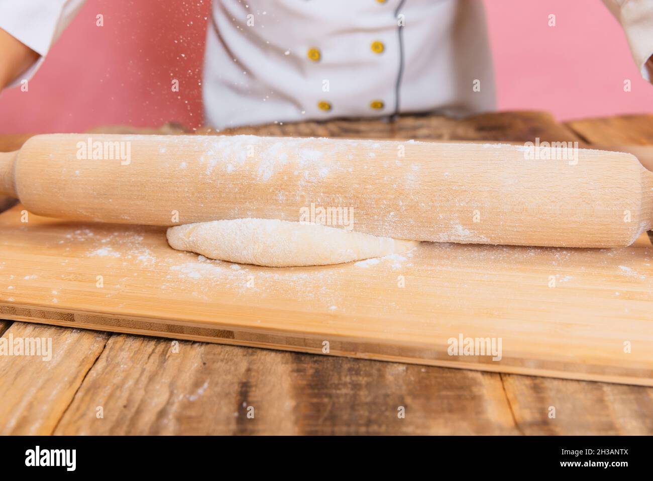 Primo piano le mani del bambino che rotolano fuori l'impasto isolato su sfondo rosa studio. Gusto, panetteria, dieta sana concetto Foto Stock