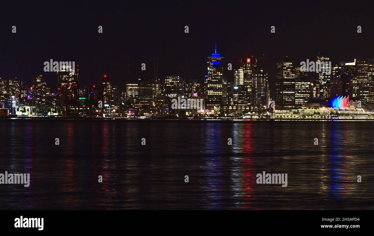 Splendida vista dello skyline di Vancouver con edifici illuminati e colorati riflessi d'acqua di notte. Foto Stock