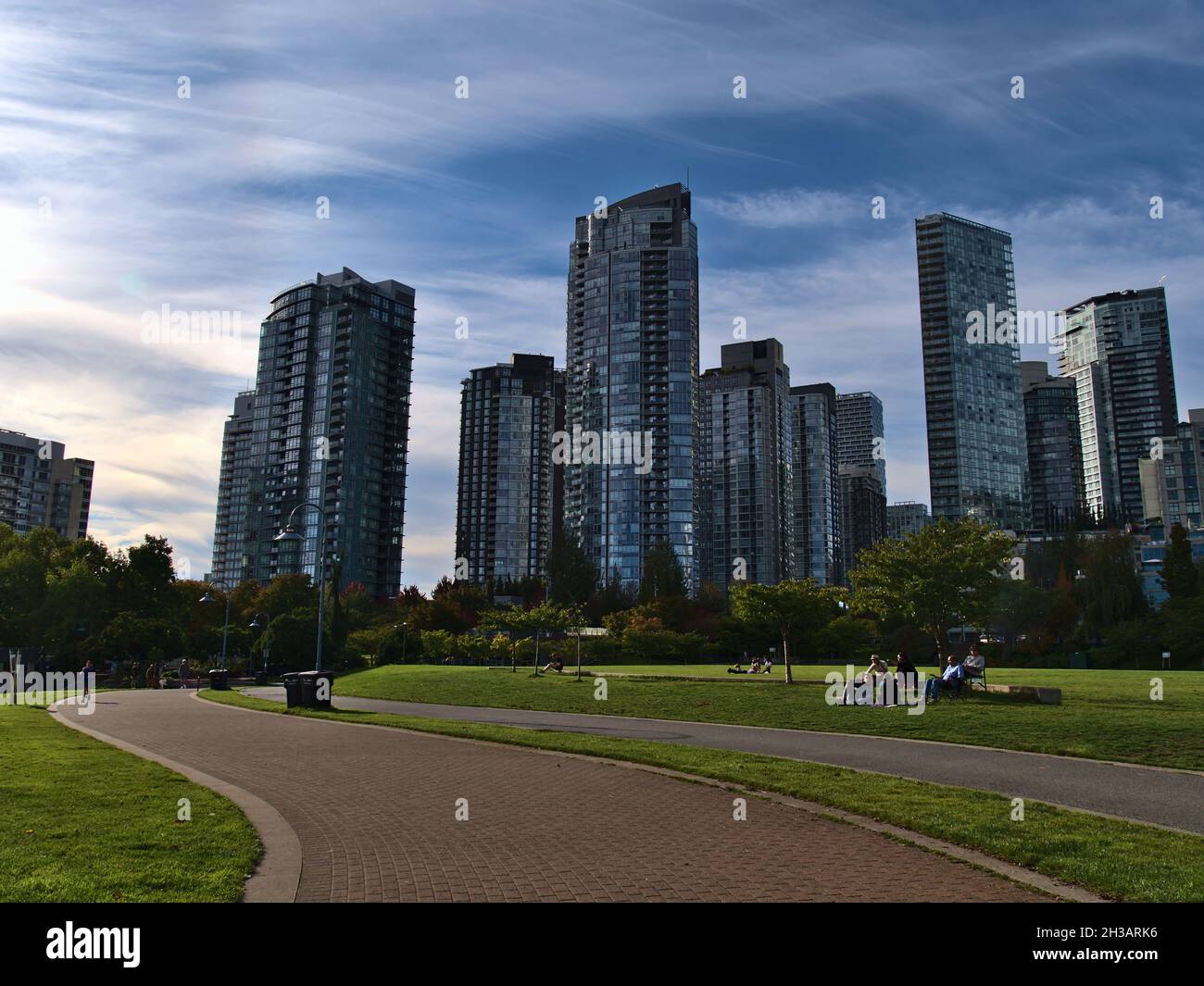 Splendida vista del David Lam Park nel centro di Vancouver a False Creek con persone che godono il sole del pomeriggio e edifici residenziali alti. Foto Stock