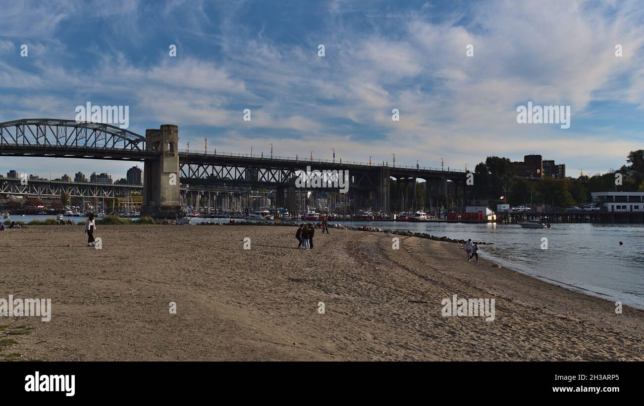 Le persone si godono il pomeriggio a Sandy Sunset Beach nel centro di Vancouver sulla riva di False Creek con Burrard Street Bridge sullo sfondo. Foto Stock