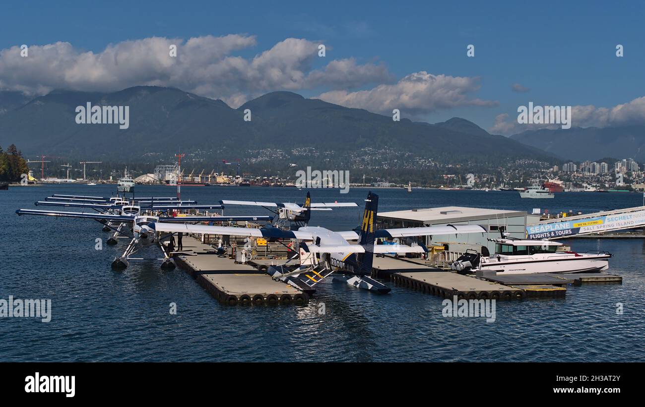 Vista degli idrovolanti allineati operati dalla compagnia aerea Harbour Air ormeggio al Vancouver Harbour Flight Center con montagne sullo sfondo. Foto Stock