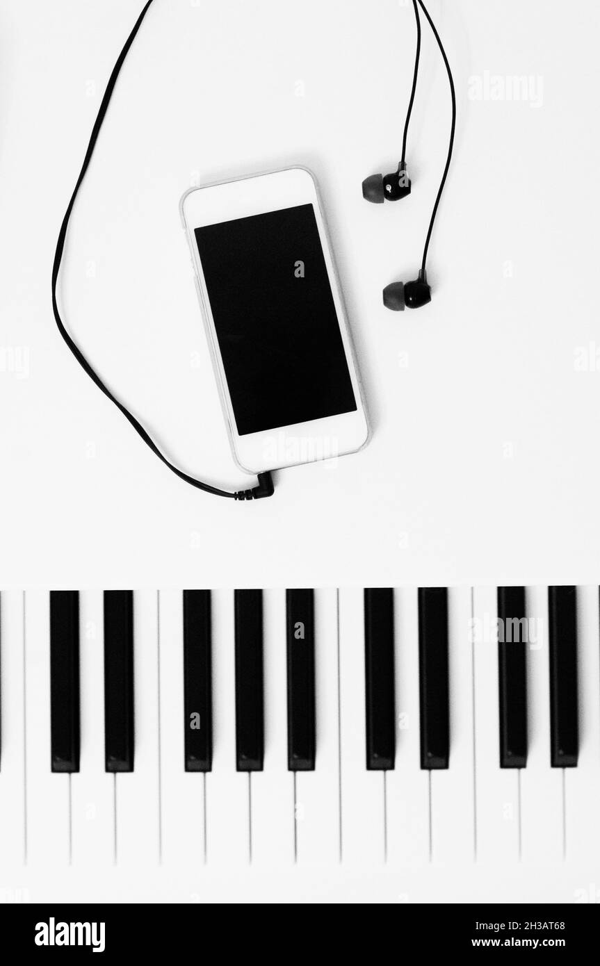 Tasti pianoforte e dispositivo di riproduzione musicale con cuffie. Foto in bianco e nero. Il concetto di tecnologie e approcci diversi nella musica. Foto Stock