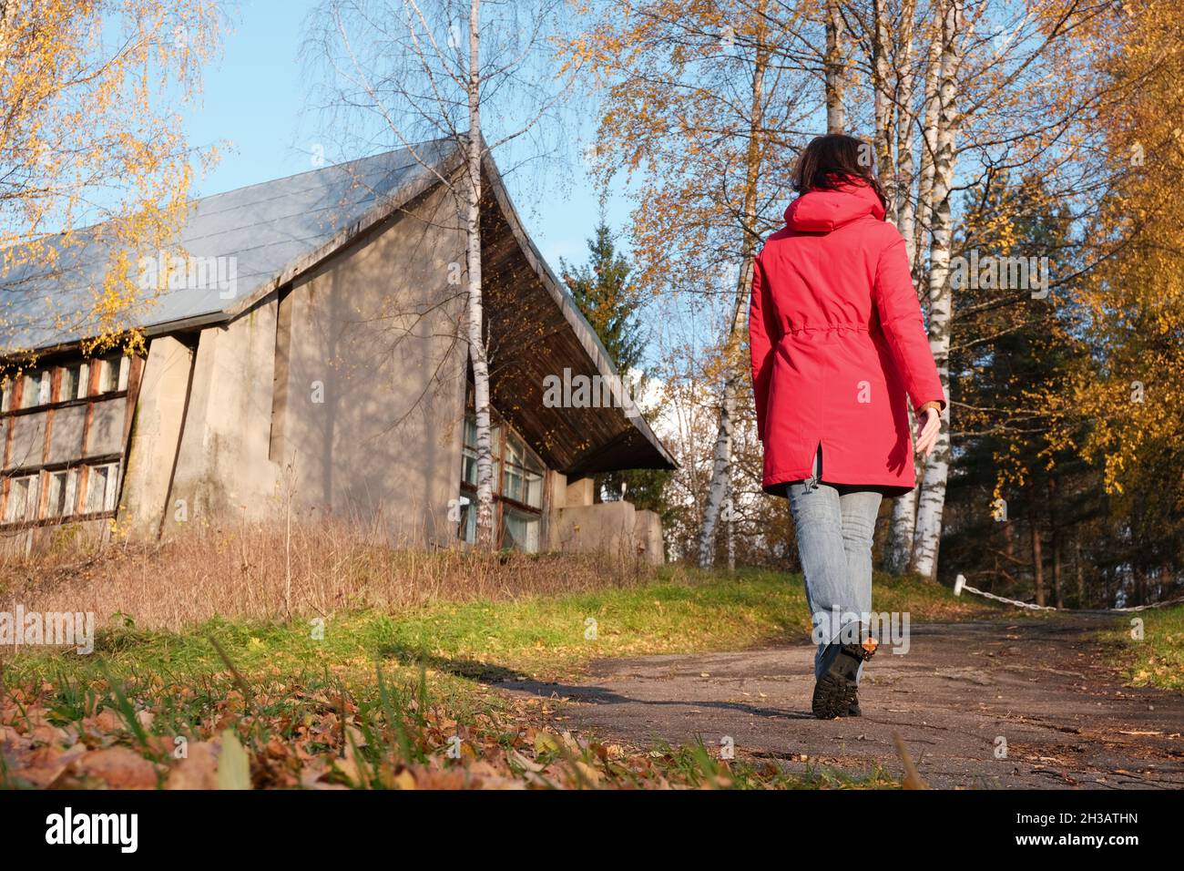 Una donna in una giacca rossa cammina attraverso il Parco d'autunno tra le foglie gialle cadute. Foto Stock