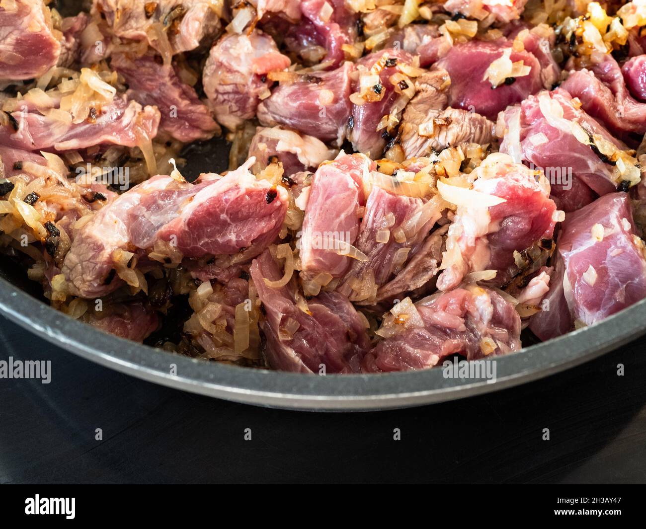 i pezzi di manzo crudo vengono fritti con cipolle tritate a spiccio in padella profonda nella cucina di casa Foto Stock