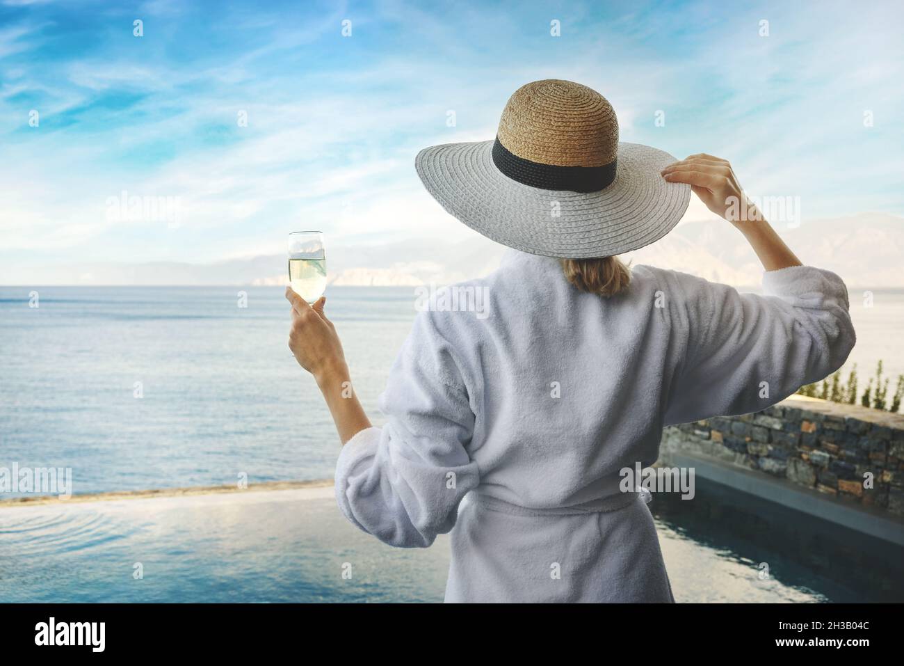 spa resort e vacanze - donna in accappatoio bianco con bicchiere di champagne in mano guardando al mare Foto Stock