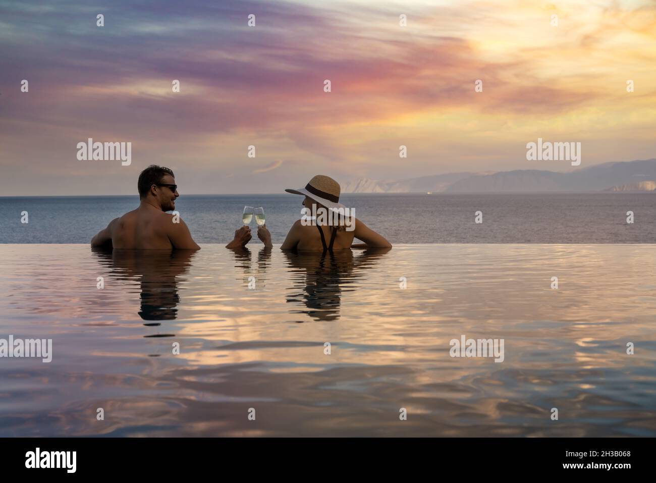 fughe romantiche - coppia bevendo champagne e godendo di un bellissimo tramonto in piscina presso il resort tropicale Foto Stock