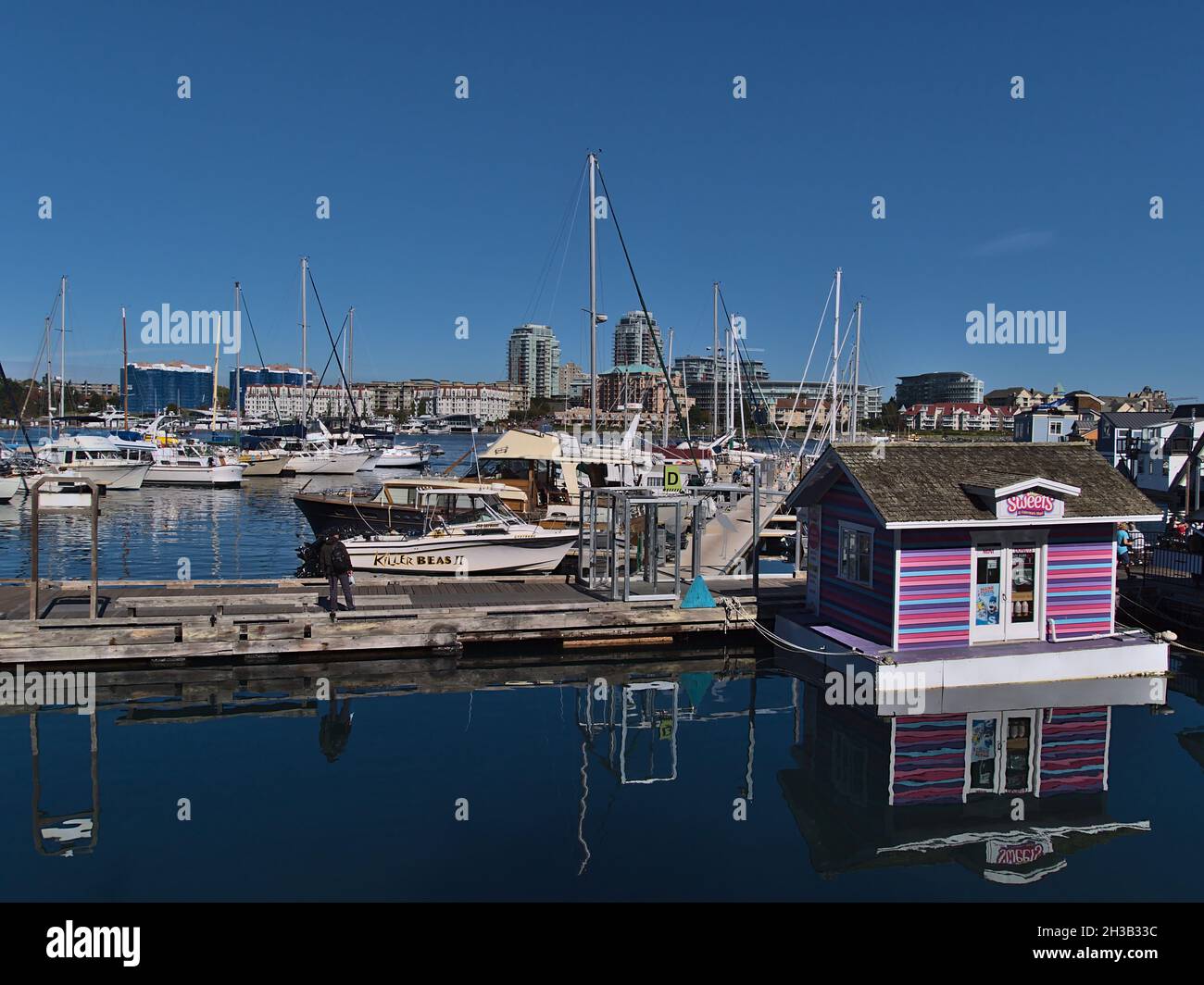 Splendida vista del Victoria Harbour con Fisherman's Wharf e porticciolo con barche a vela in giornata di sole con skyline e colorato edificio galleggiante. Foto Stock
