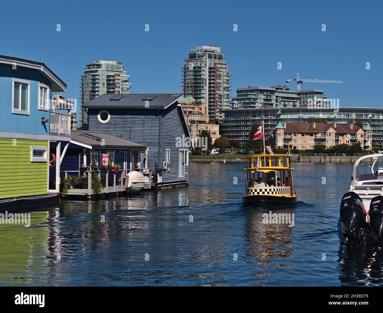 Piccolo traghetto Victoria Harbour con partenza da Fisherman's Wharf con case galleggianti colorate e skyline sullo sfondo in una giornata di sole. Foto Stock