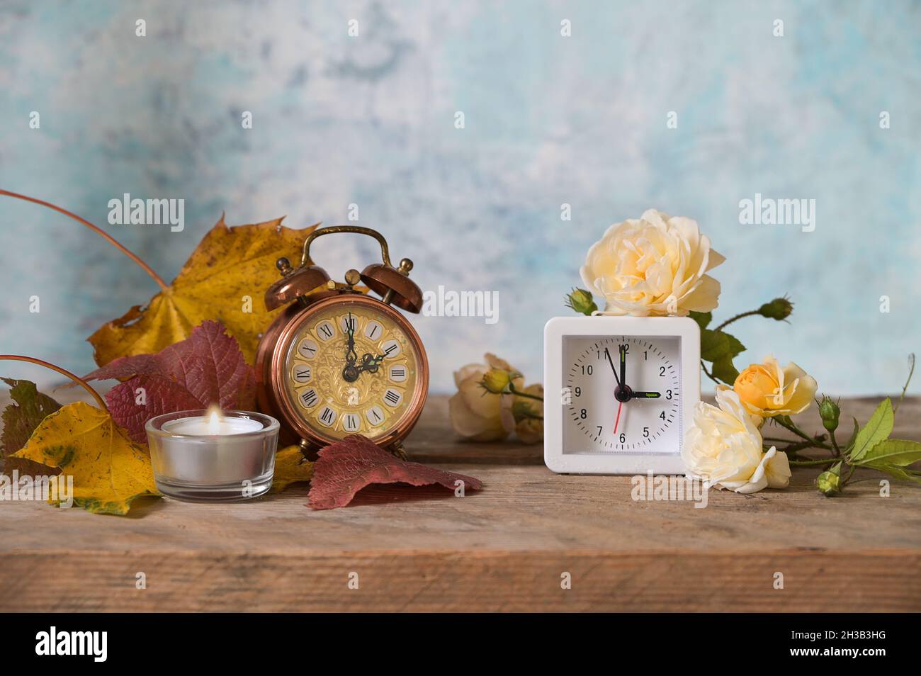 Cambio orologio, due sveglie, stile retrò e moderno, che mostra l'ora invernale e l'ora estiva, foglie autunnali e fiori in legno rustico, retro blu chiaro Foto Stock