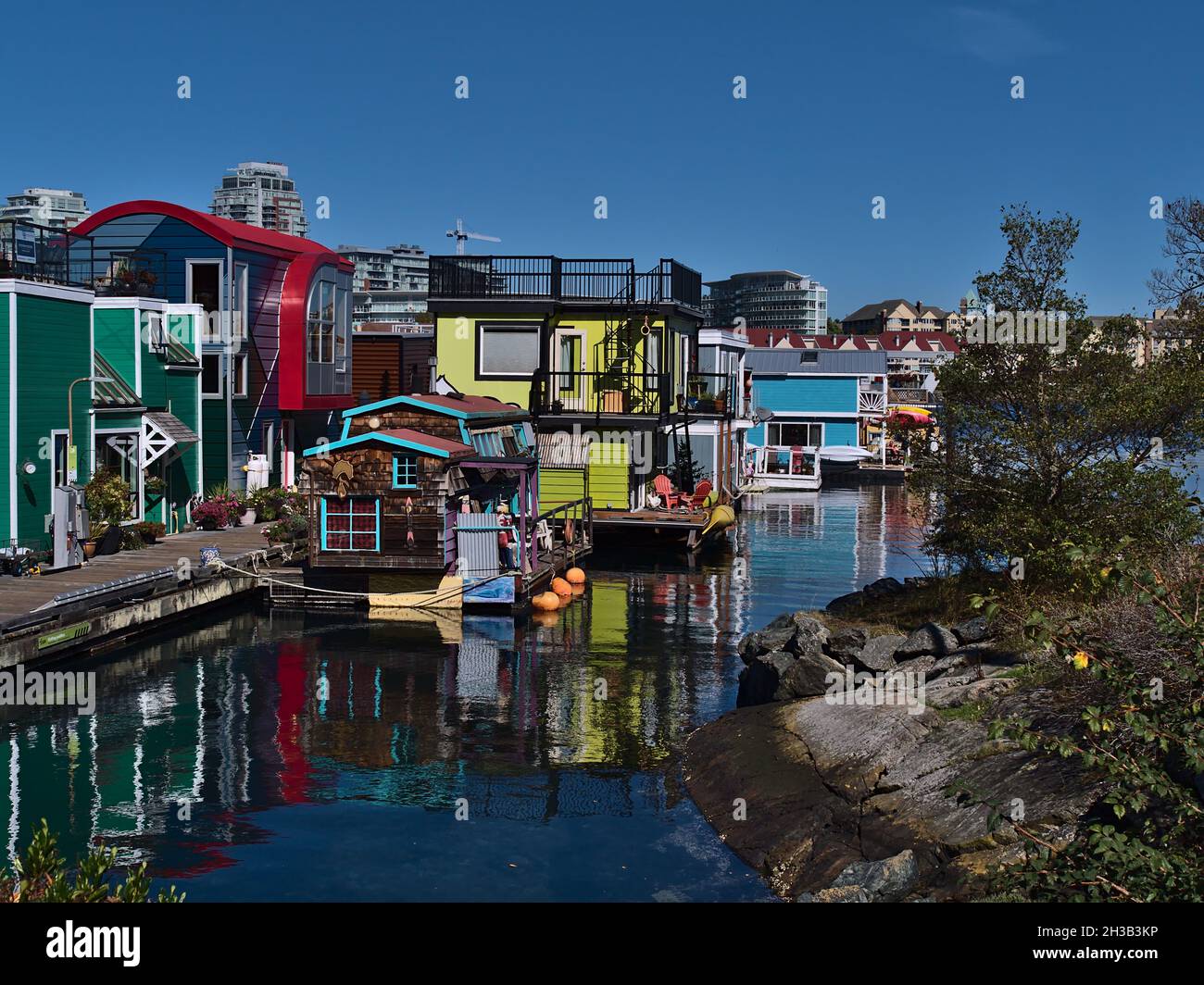 Colorate case galleggianti di Fisherman's Wharf a Victoria Harbour, Vancouver Island in una giornata di sole in autunno con riflessi sulla superficie dell'acqua. Foto Stock