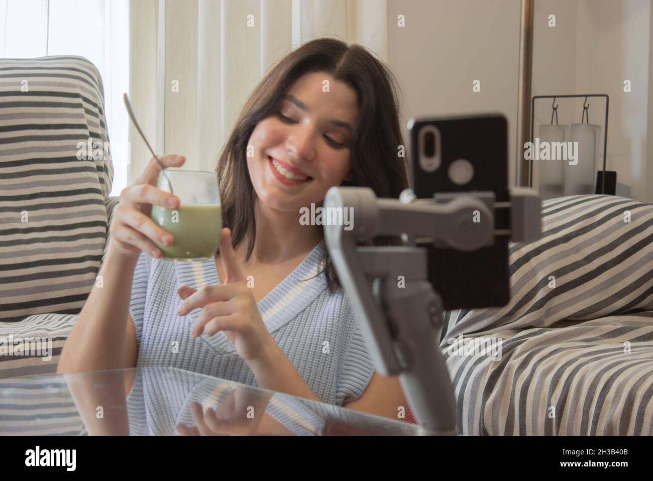 Ragazza blogger filma video online da condividere sui suoi social network parlando con i seguaci circa i benefici del tè matcha. Concetto di benessere. Foto Stock