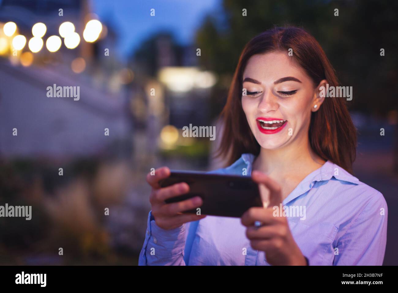 Giovane donna rossa caucasica che ride nello smartphone di notte in città Foto Stock