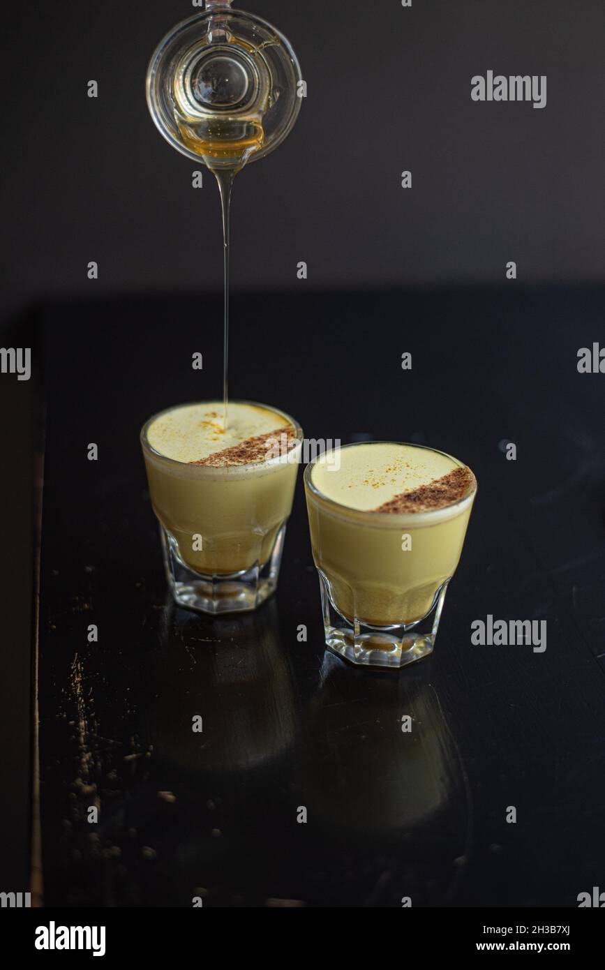 Due eleganti bicchieri di latte dorato in bicchieri gibilterra sormontato da cannella, mentre il barista rigna la cannella in cima. Foto Stock