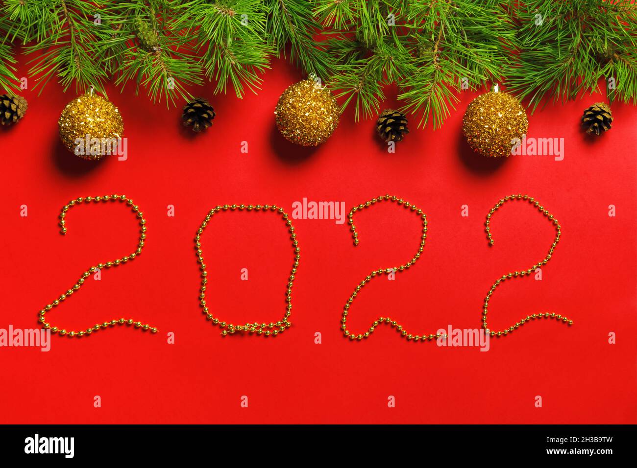 Anno nuovo 2022. Banner natalizio fatto di rami di abete con coni e palline su sfondo rosso. Iscrizione bead. Foto Stock