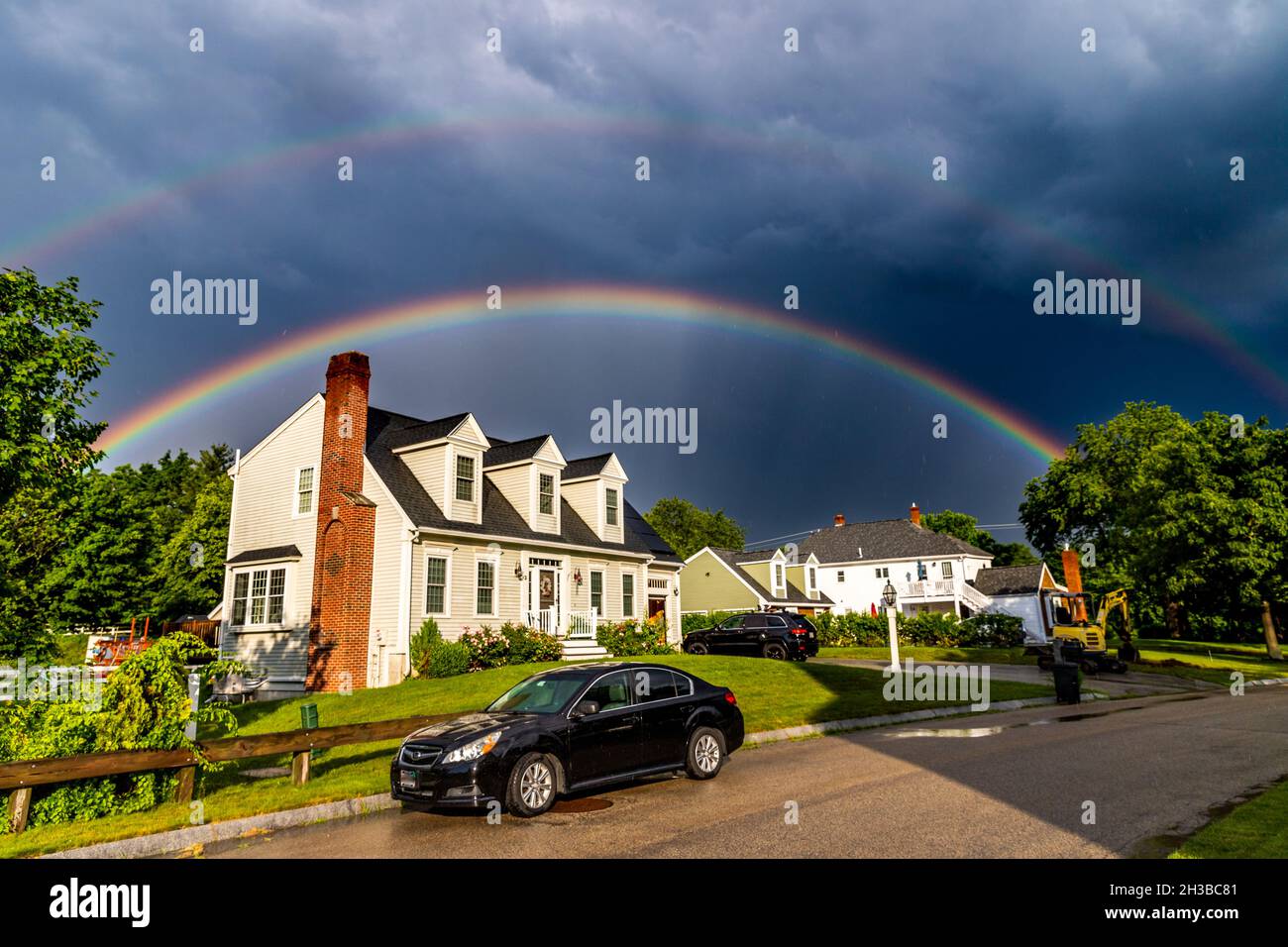 Fenomenale doppio arcobaleno che brilla sopra casa sotto un cielo drammatico. Foto Stock