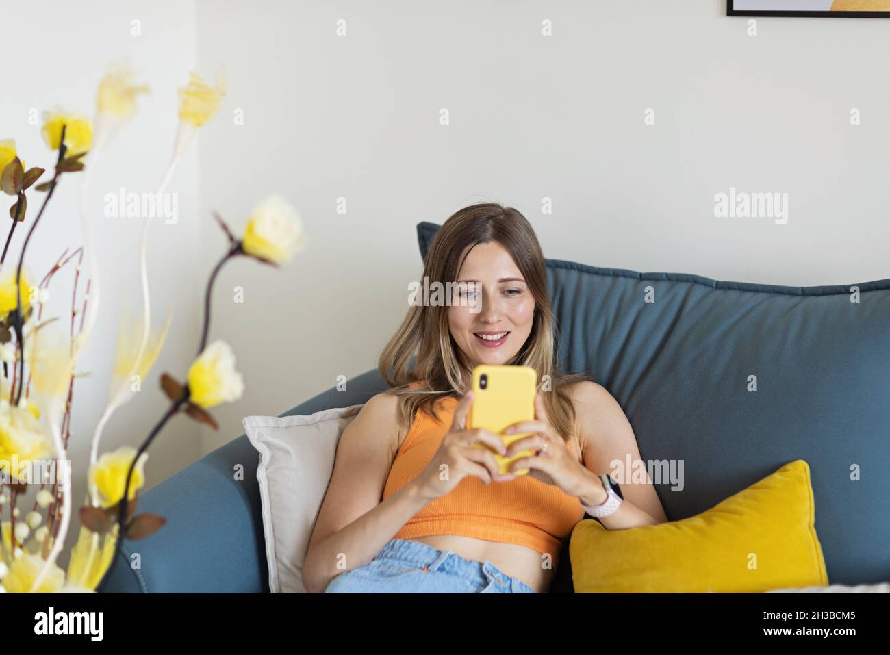 Felice giovane bionda caucasica donna rilassarsi a casa da solo, seduta sul divano in comoda posa, blogger condividere buone notizie sui social media via mobile Foto Stock