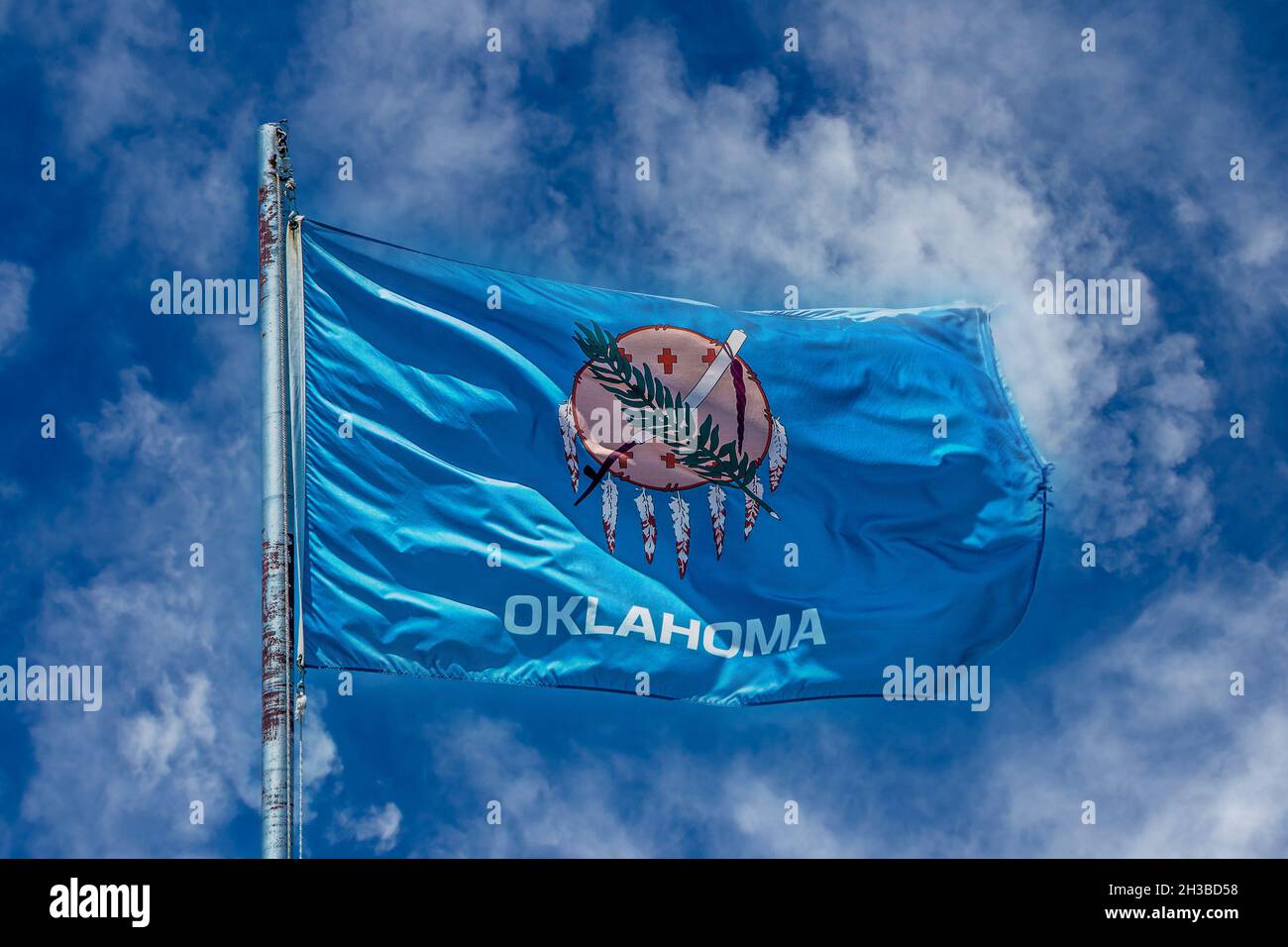 Bandiera di Stato dell'Oklahoma su palo arrugginito che soffia nel vento di fronte al bel cielo nuvoloso blu chiazzato. Foto Stock
