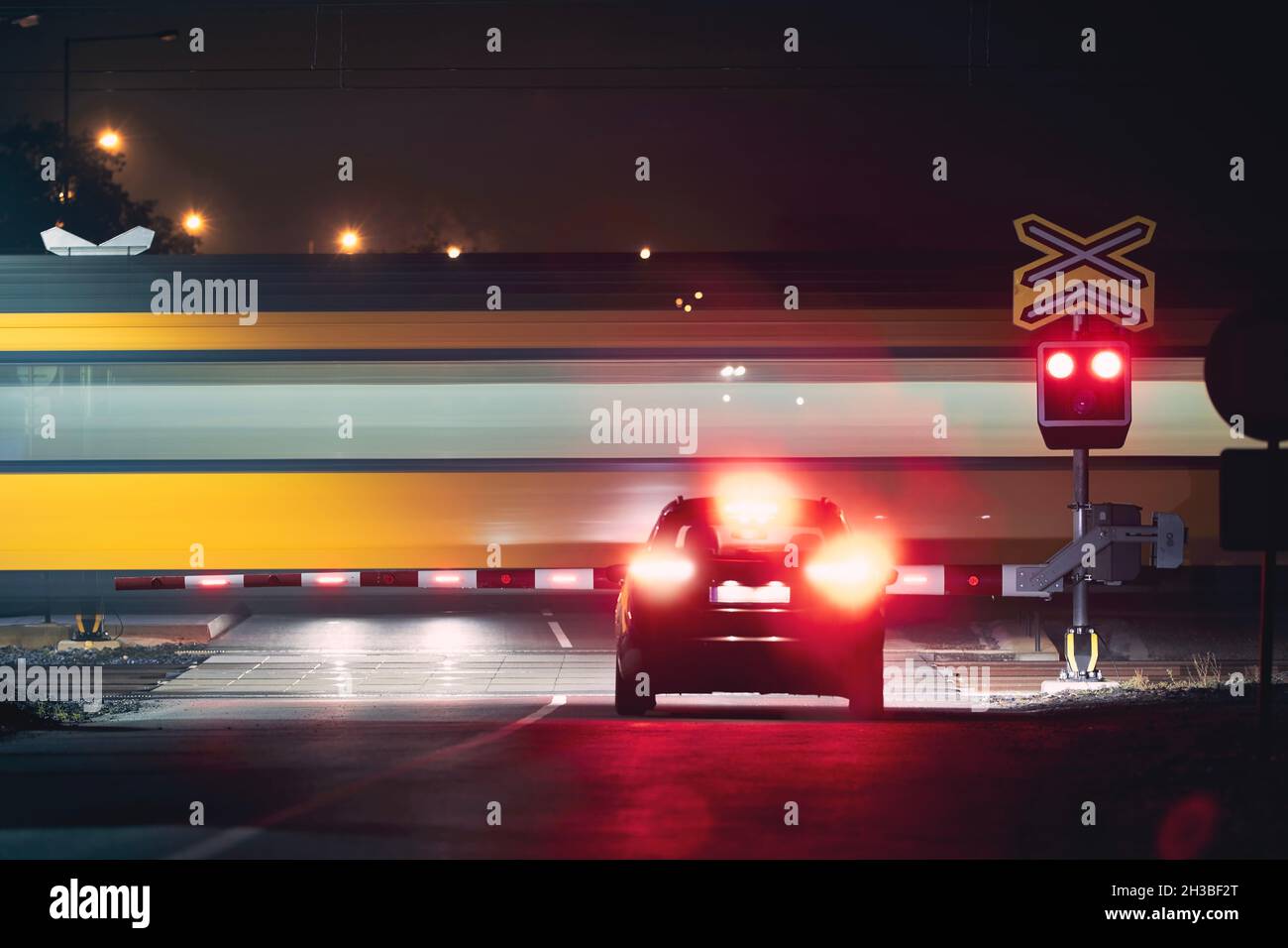 Ferrovia di notte. Treno passeggeri che passa per attraversamento ferroviario mentre le spie rosse arrestano l'auto Foto Stock
