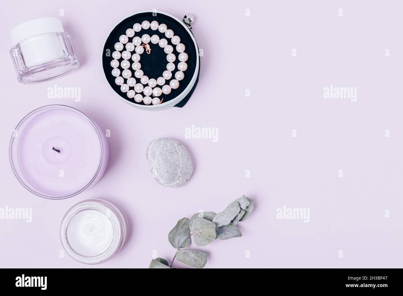 Composizione a posa piatta femminile con moisturizer, collana a candela e perla su sfondo chiaro con spazio per la copia. Foto Stock
