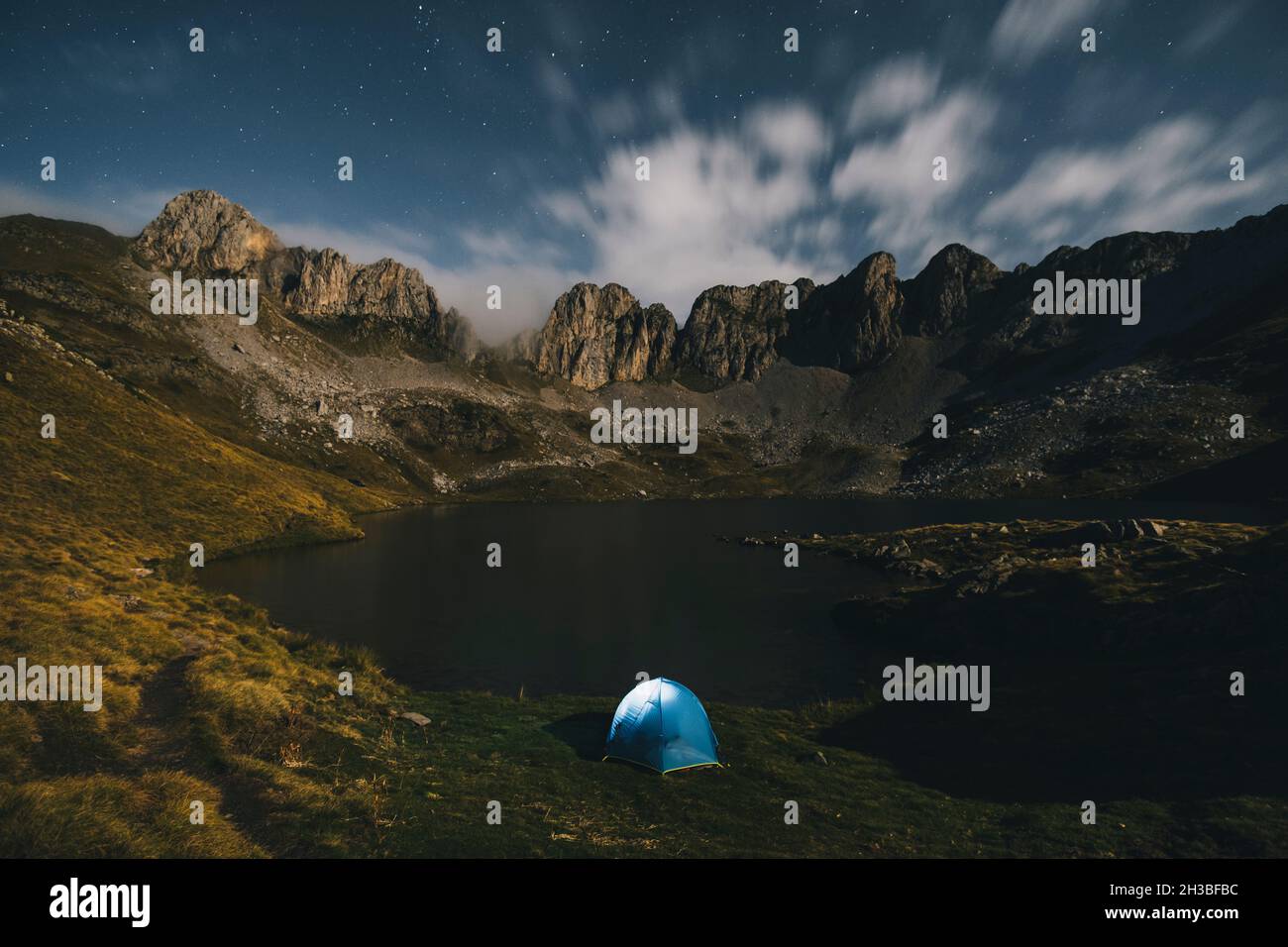 Tenda illuminata contro montagne aspre e lago, Pirenei. Foto Stock