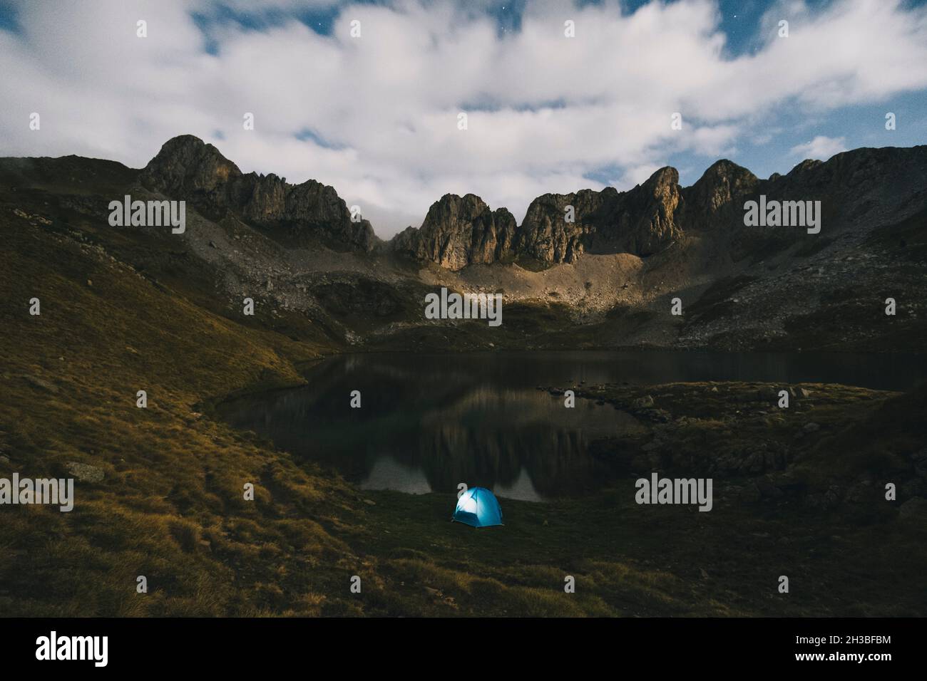 Tenda illuminata contro montagne aspre e lago, Pirenei. Foto Stock