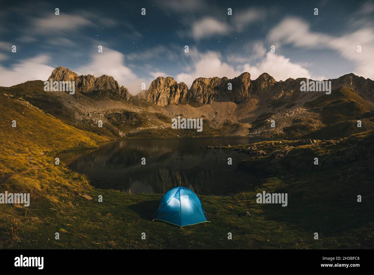 Tenda illuminata contro montagne aspre e lago, Pirenei. Foto Stock
